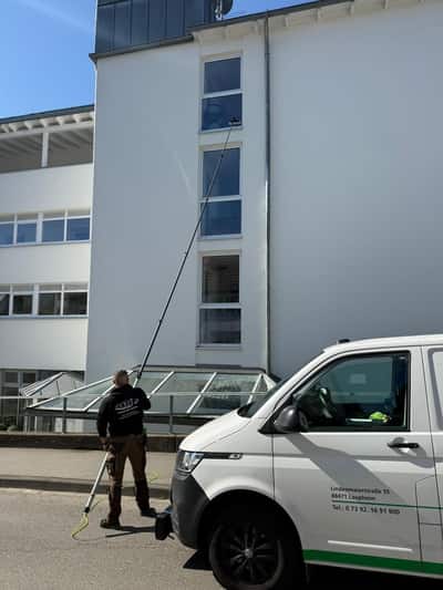 Mitarbeiter reinigt die Fenster eines Mehrfamilienhauses mit einer Teleskopstange