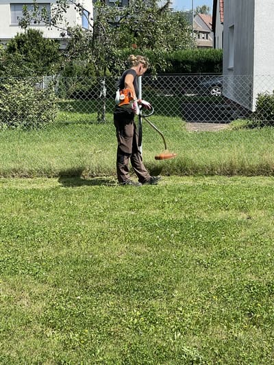 Mitarbeiter von Jakob's Dienstleistungen mäht mit der Motorsense entlang einer Rasenkante